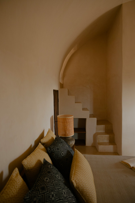 Dettaglio di una suite con letto matrimoniale, scala interna in muratura e soffitti a volta, caratterizzata da materiali naturali e atmosfera accogliente.