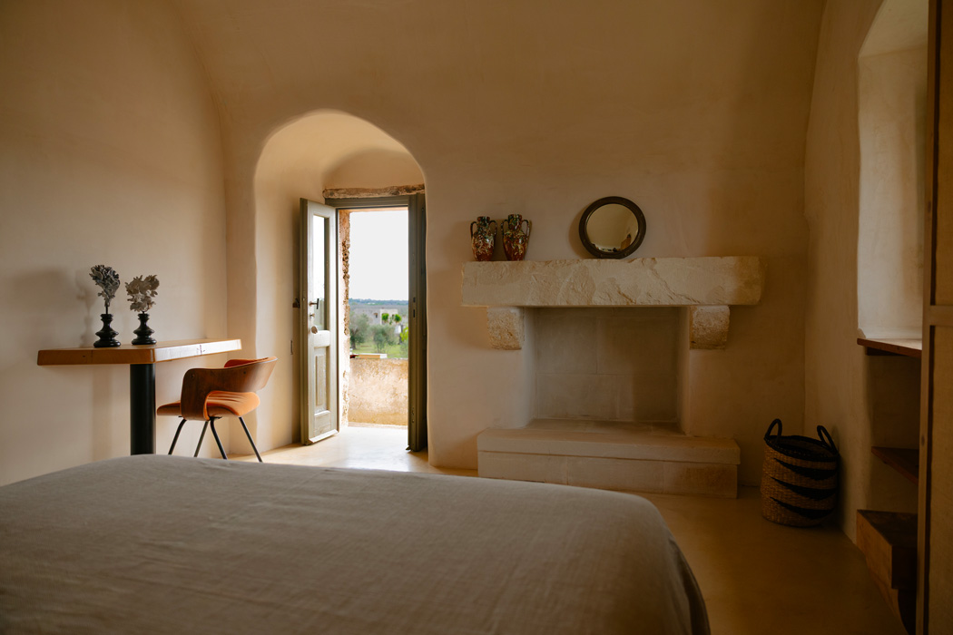 Suite con camino in pietra, letto matrimoniale, soffitti a volta e accesso diretto verso l’esterno con vista sulla campagna.