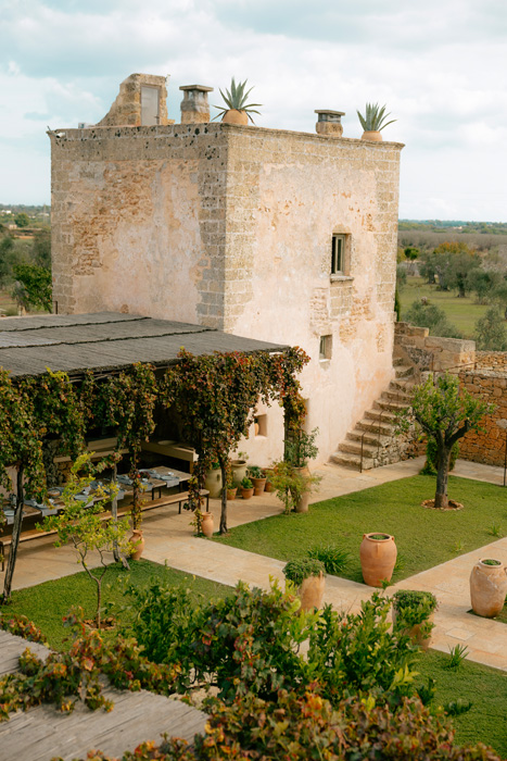 Vista dall’alto della corte interna della masseria con giardino, pergolato e antica torre in pietra.