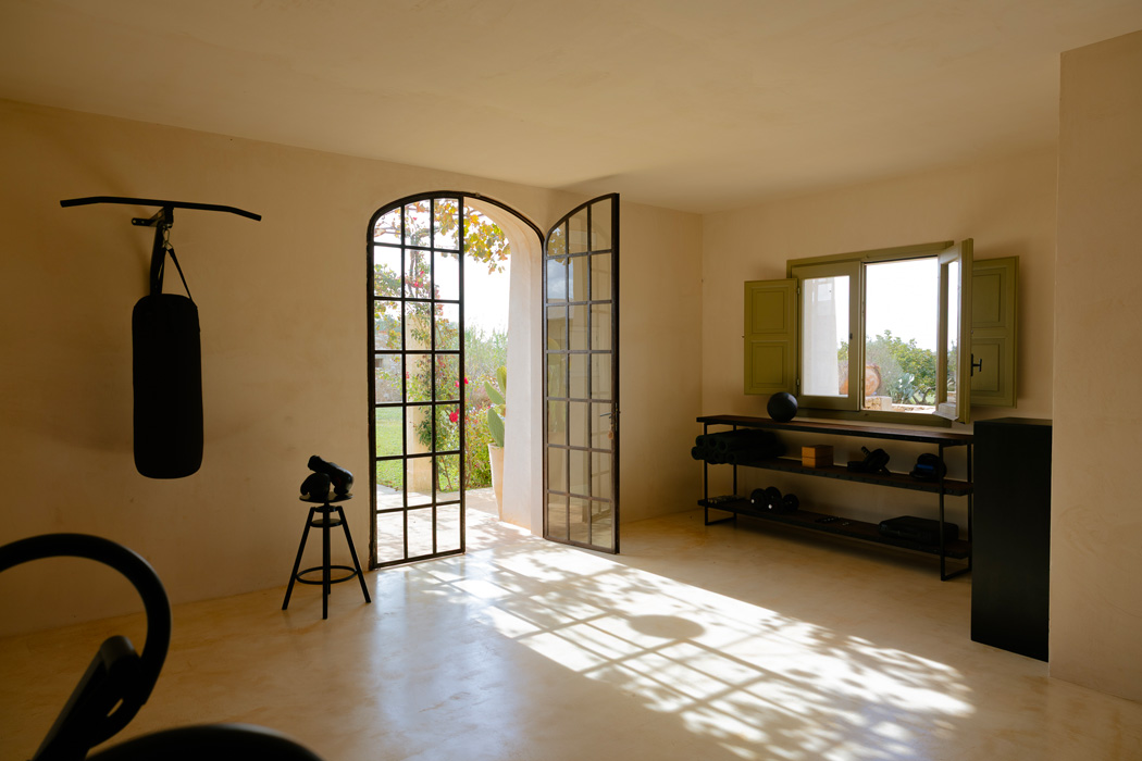 Sala fitness minimalista con attrezzature wellness, grandi aperture e luce naturale.