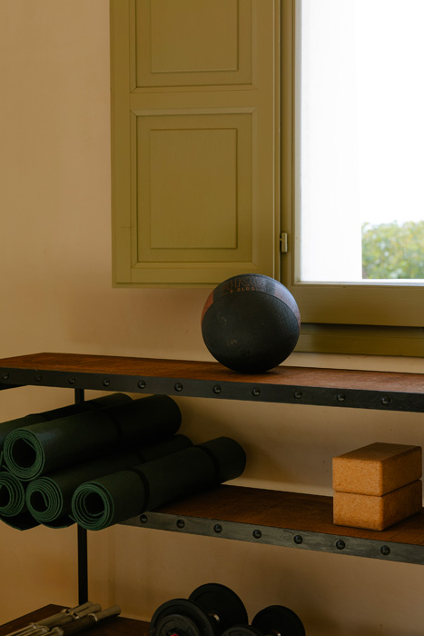 Dettaglio dell’area palestra con tappetini yoga, pesi e attrezzature wellness minimaliste.