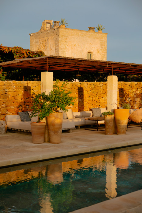 Piscina della masseria illuminata dalla luce del tramonto con area lounge e pietra naturale.