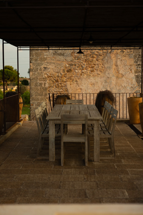 Terrazza coperta con tavolo in legno e pareti in pietra in stile mediterraneo.