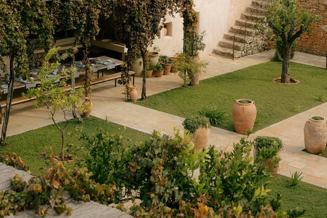 Corte esterna con giardino curato, alberi, pergolato e dettagli in pietra naturale.
