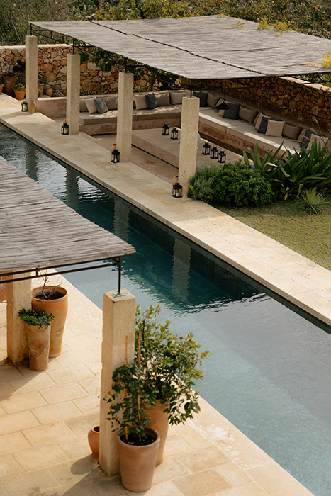 Piscina con area relax e lounge all’aperto circondata da pietra naturale e vegetazione mediterranea.