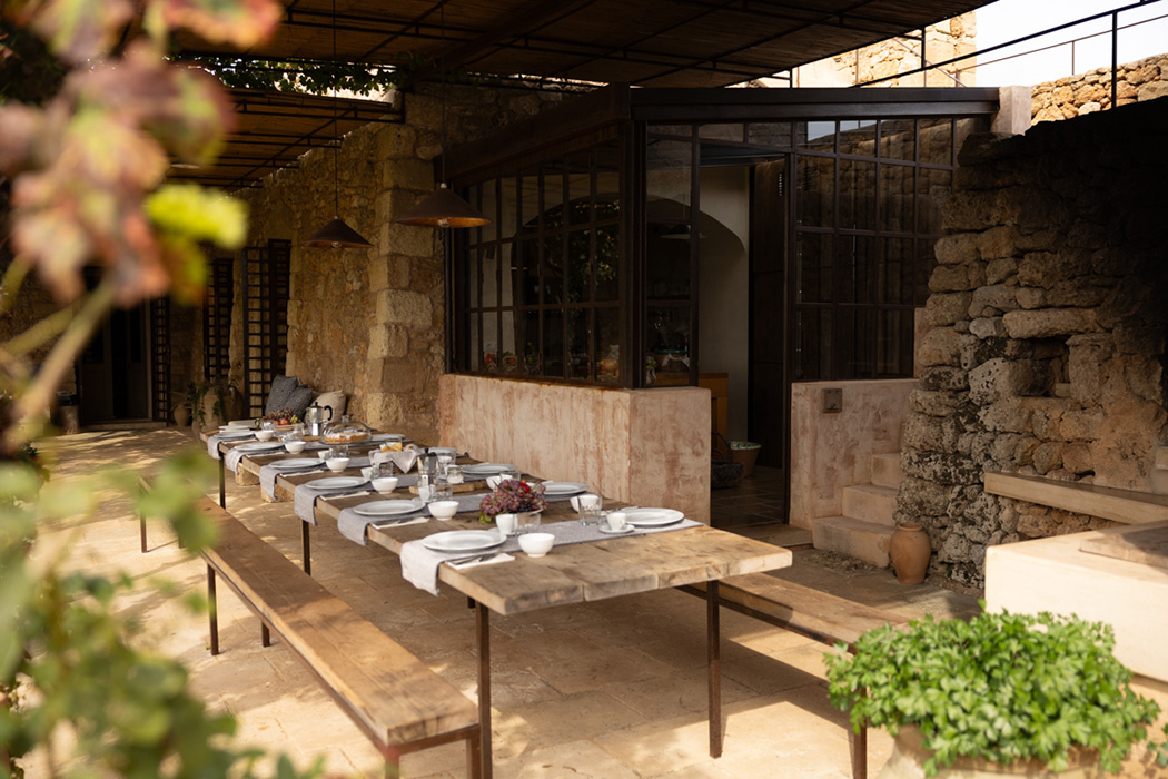 Tavolo apparecchiato all’aperto in una corte in pietra con atmosfera rustica ed elegante.