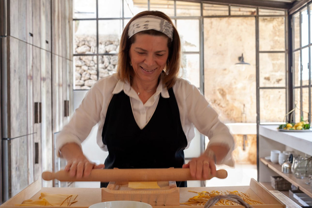 Donna mentre prepara pasta fresca fatta a mano in una cucina luminosa dal design mediterraneo.