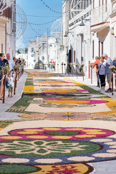 Strada decorata con tappeti floreali colorati durante la tradizione dell’infiorata in un borgo salentino.
