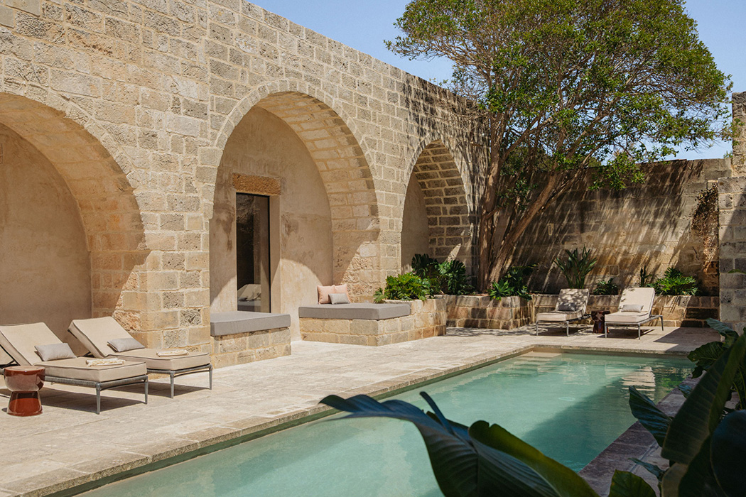 Piscina esterna circondata da archi in pietra e vegetazione mediterranea.